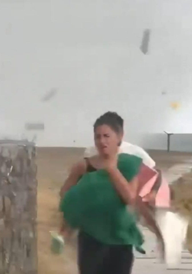 Woman running with child close to camera as objects fly behind. CAMPANIA, ITALY: THIS FOOTAGE shows the alarming moments a waterspout caused chaos in Italy on August 19, and could¿ve been the aftermath of the same freak weather incident which caused tycoon Mike Lynch's hired yacht to sink. The footage shows beachgoers running for their lives as a powerful waterspout moves on land in the Policastro, Campania region of Italy and causes damage in Italy on August 19th 2024. In this video a beaching facility from where several kinds of objects were lifted into the air, nobody on land was harmed. There were 18 confirmed waterspouts off the coasts of Italy on August 19th, some were powerful waterspouts, like the one in this video, one of which may have been responsible for the sinking of a large yacht off of Sicily. According to vessel tracking app Vesselfinder, the boat embarked from the Sicilian port of Milazzo on 14 August and was last tracked east of Palermo on Sunday evening, with a navigation status of "at anchor". The ship was struck by a tornado over the water, known as a waterspout, causing the Bayesian yacht to capsize. Specialist divers continue to search for six people who were on board a luxury superyacht which capsized off the coast of Sicily on Monday morning. The boat had a crew of 10 people and 12 passengers. The vessel's cook, Recaldo Thomas, has died and his body has been recovered, according to Sicily's civil protection agency. 15 people have been rescued from the boat, while six remain missing. Specialist divers from the Italian fire brigade resumed their search early on Tuesday morning. A spokesperson for the UK Foreign Office said: ¿We are providing consular support to a number of British nationals and their families following an incident in Sicily, and are in contact with the local authorities.¿ The Italian coastguard said on the morning of the yacht discovery: ¿This morning at about 5am, following a violent storm, a 56-metre yacht called Bayesian flying the British flag sank near Porticello.¿ mediadrumimages