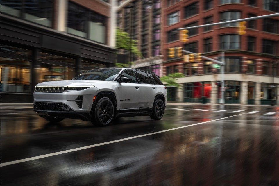 a white jeep is driving down a wet city street