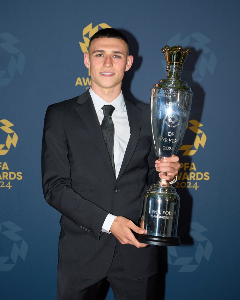 a man in a suit is holding a trophy that says phil foden manchester city