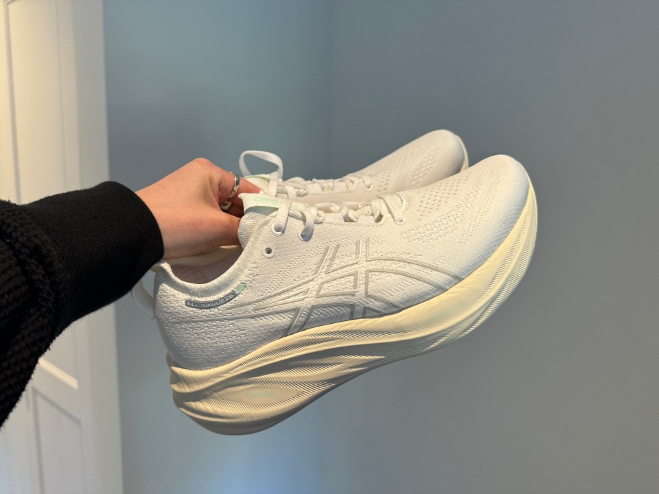 a person is holding a pair of white asics shoes