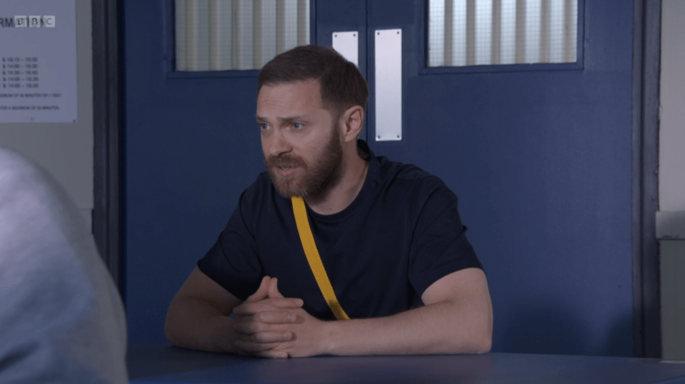 a man sits at a table in front of a sign that says bbc