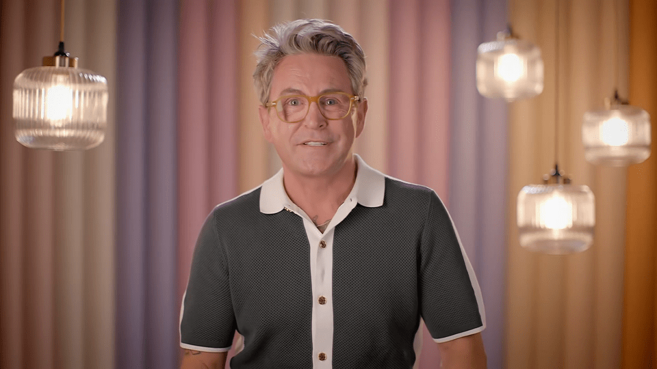 a man wearing glasses stands in front of a rainbow curtain