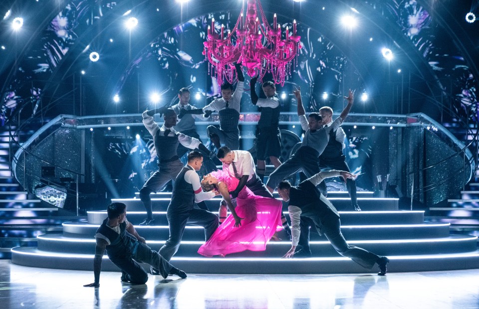 a woman in a pink dress is surrounded by men on a stage