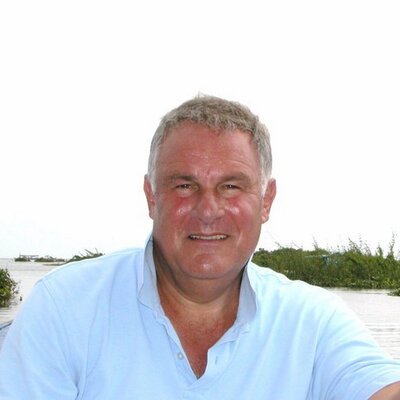 a man in a blue shirt is sitting in front of a body of water .