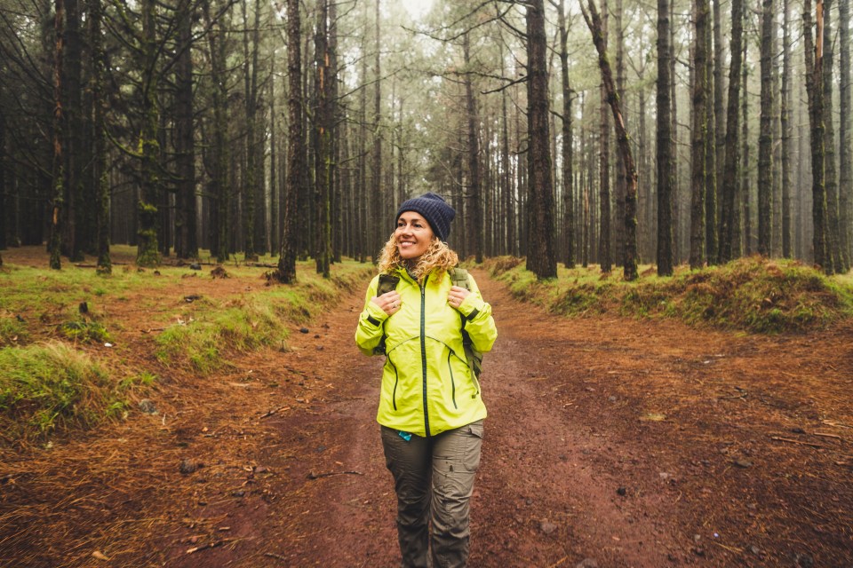 a woman in a yellow jacket is walking through a forest