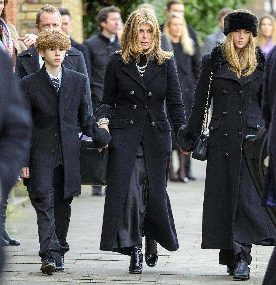 three people in black coats are walking down a street
