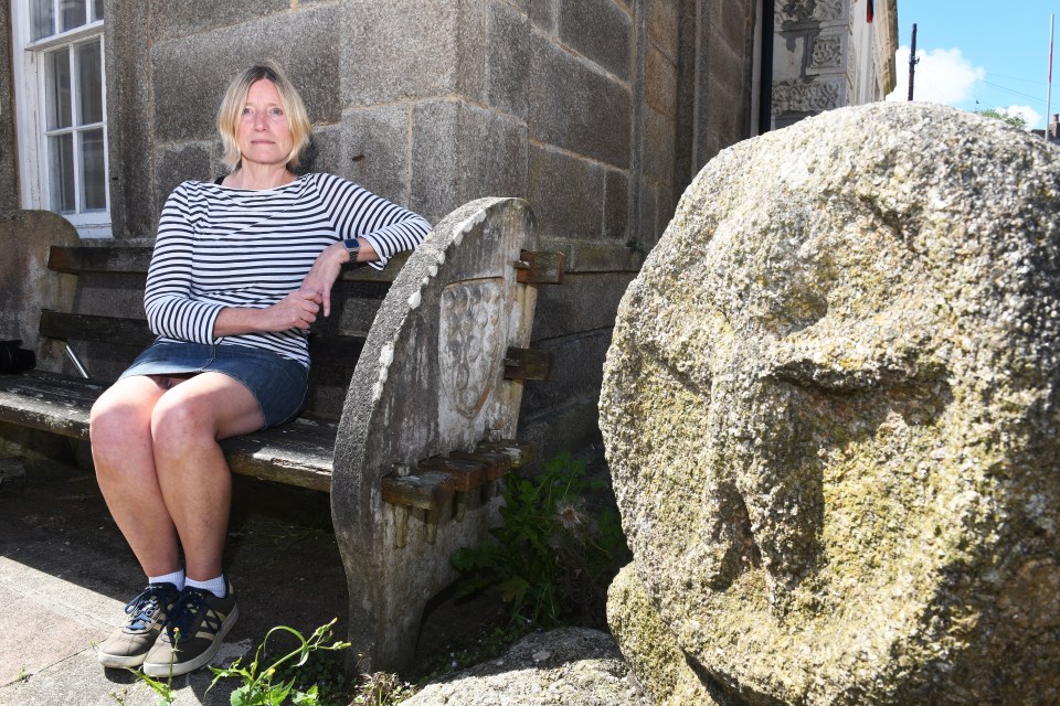a woman sits on a bench next to a large rock