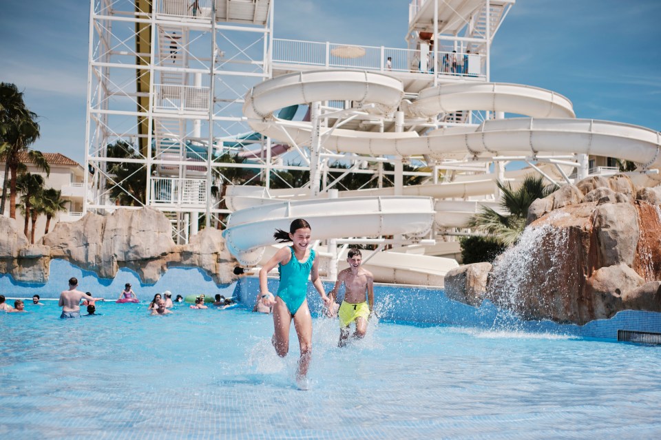 a girl in a blue swimsuit is running towards a water slide