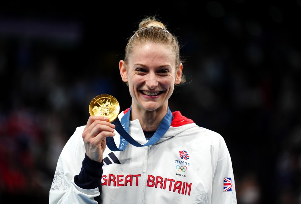 a woman in a great britain jacket holds a gold medal