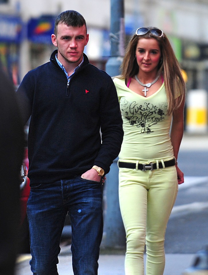 a man and a woman are walking down a street and the woman is wearing a guess shirt