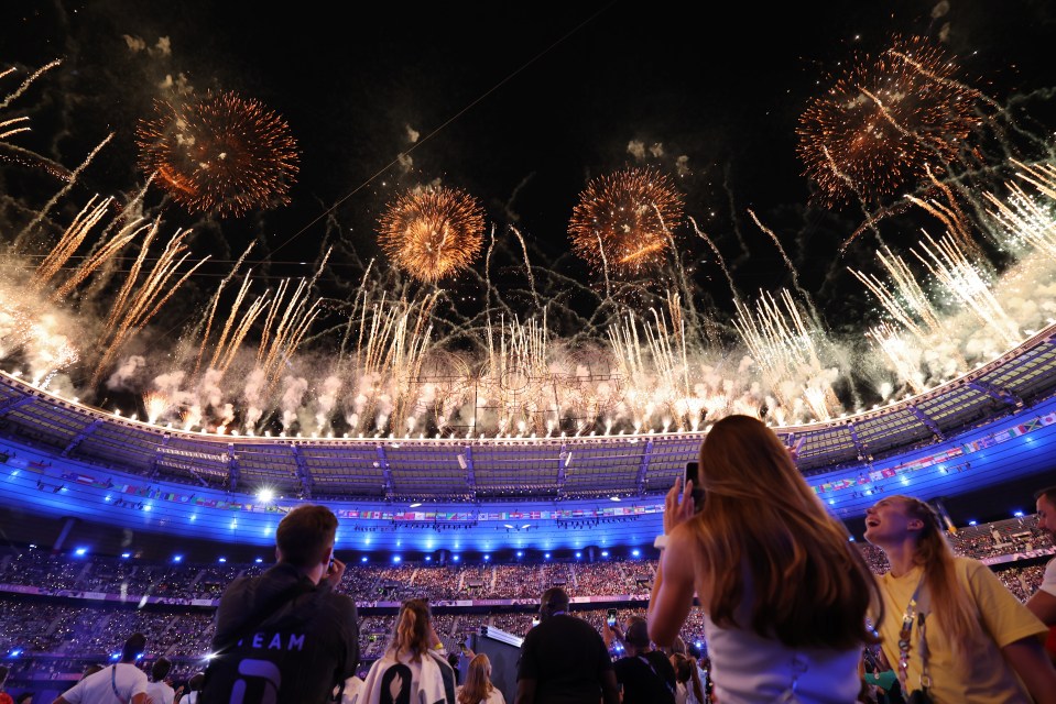 a woman taking a picture of fireworks in a stadium with the word team on her back