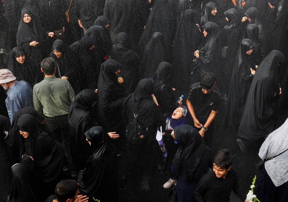 A girl reacts as it rains during the funeral procession in Tehran