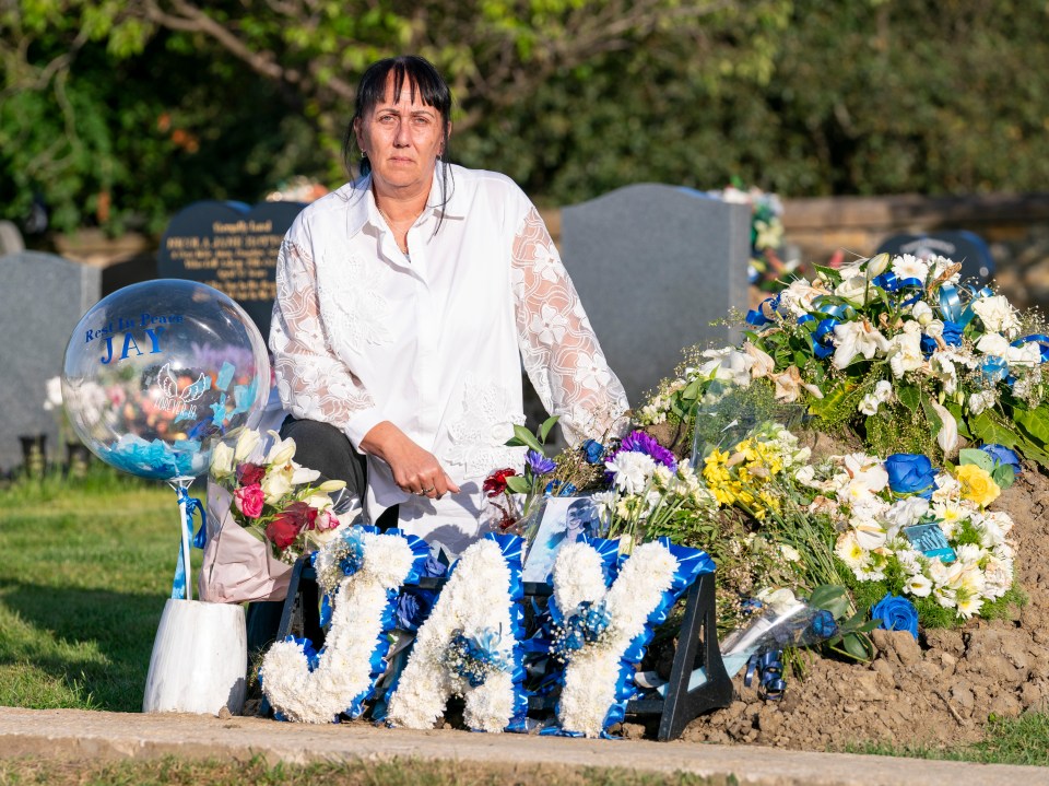 a woman sits in front of a grave with flowers and a sign that says jay