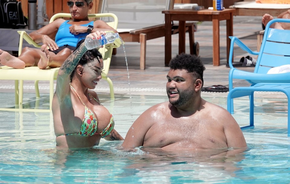 a woman in a bikini pours water on a man in a pool