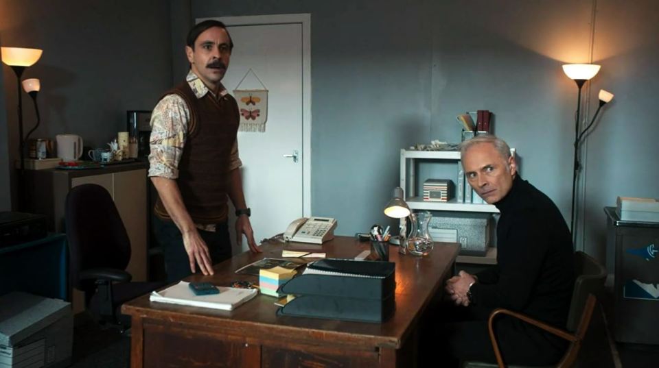 a man standing next to a man sitting at a desk