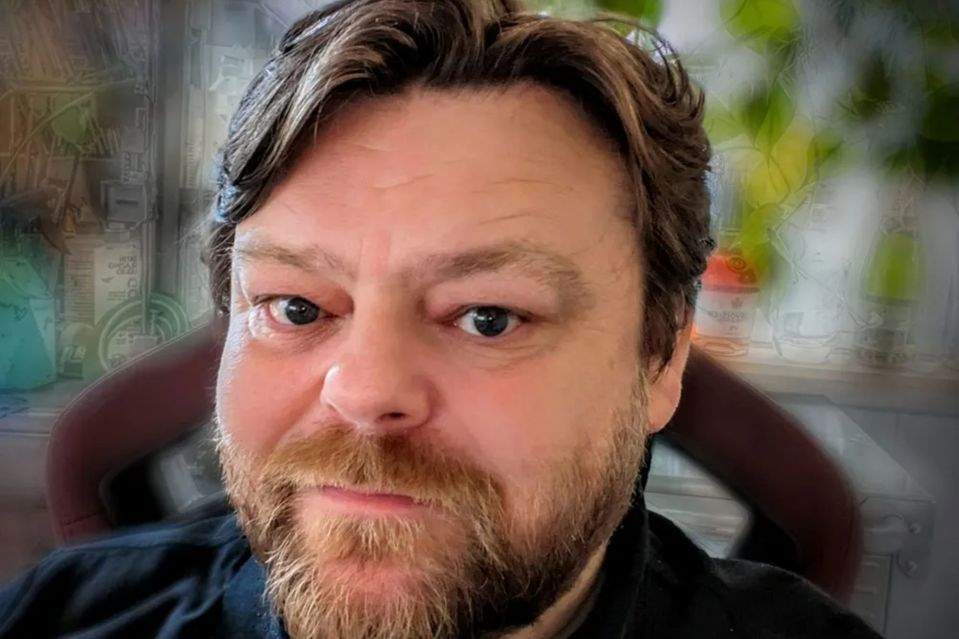 a man with a beard and a black shirt looks at the camera