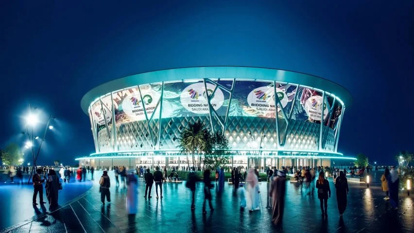 Night view of a futuristic stadium lit up, with "Bidding Nation Saudi Arabia" displayed on its exterior.