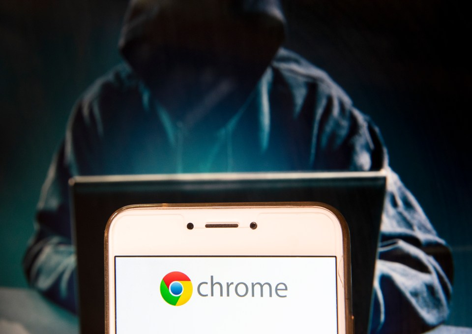 Photo illustration of a smartphone displaying the Chrome logo, with a blurred image of a hooded figure using a laptop in the background.