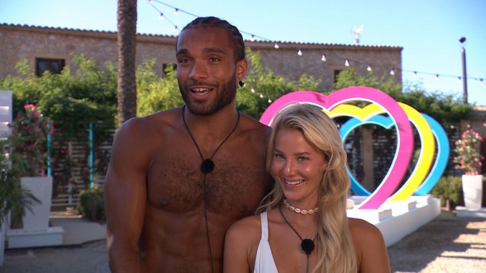 a man and a woman standing in front of a heart shaped sign