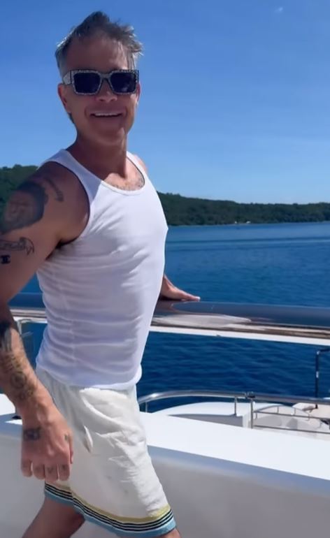 a man wearing sunglasses and a white tank top is standing on a boat .