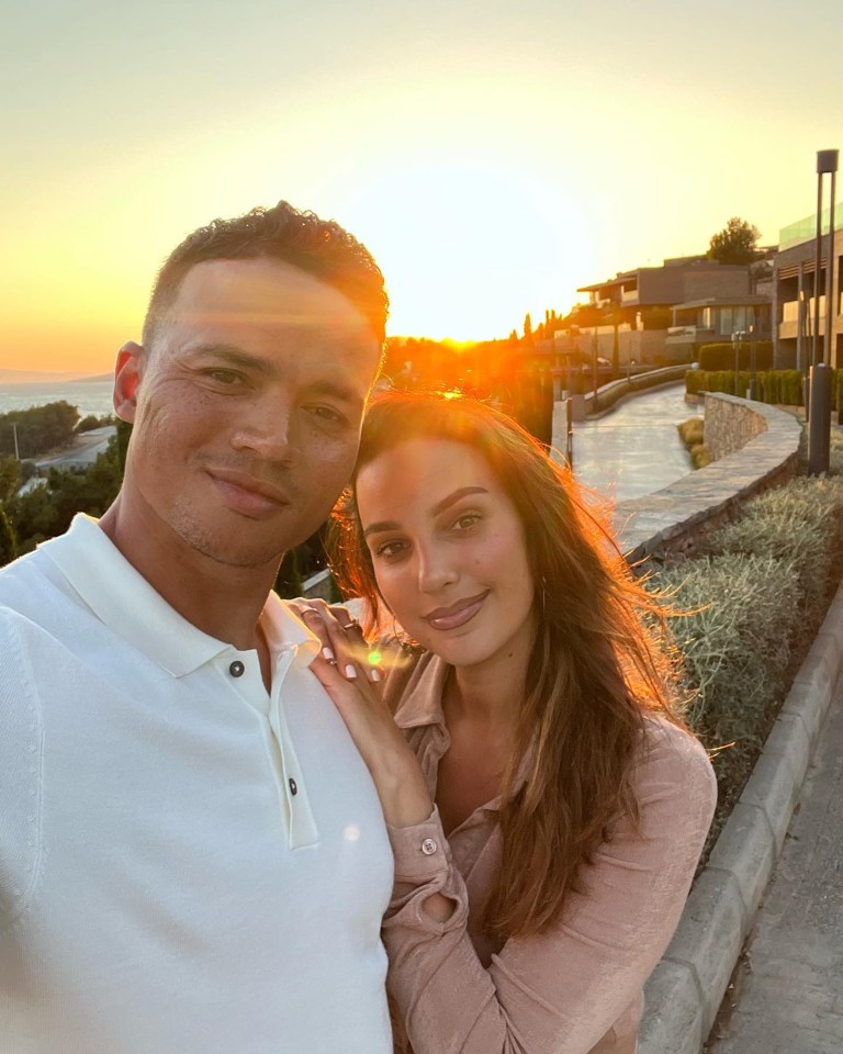 a man and a woman pose for a picture with the sun setting in the background