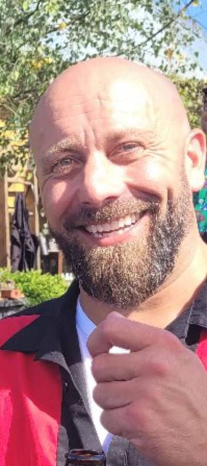 a bald man with a beard is smiling and holding a bottle of beer .