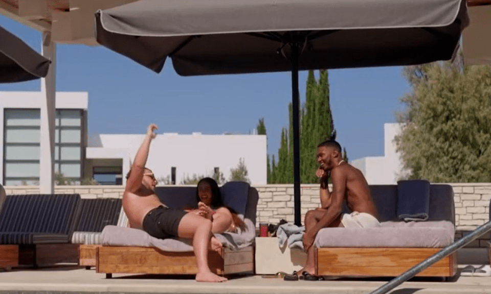 two men and a woman sit on lounge chairs near a pool