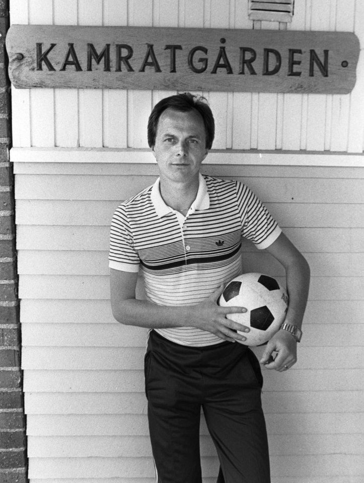 a man holding a soccer ball in front of a sign that says kamratgarden