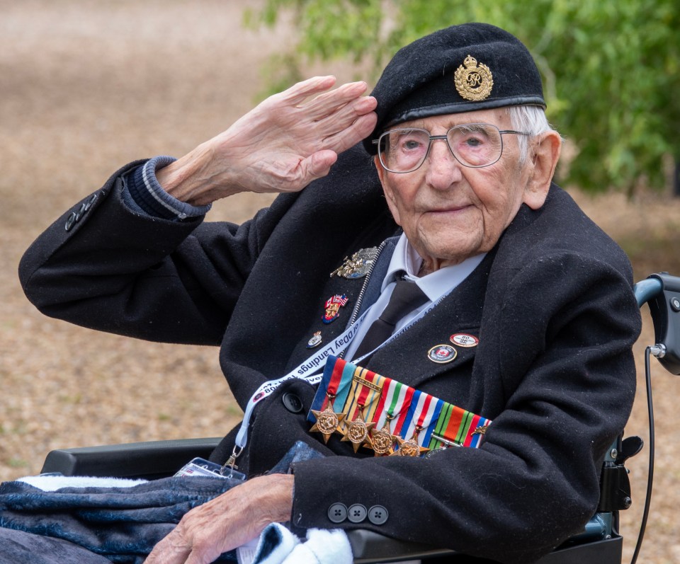 a man in a wheelchair salutes while wearing a badge that says ' british legion ' on it