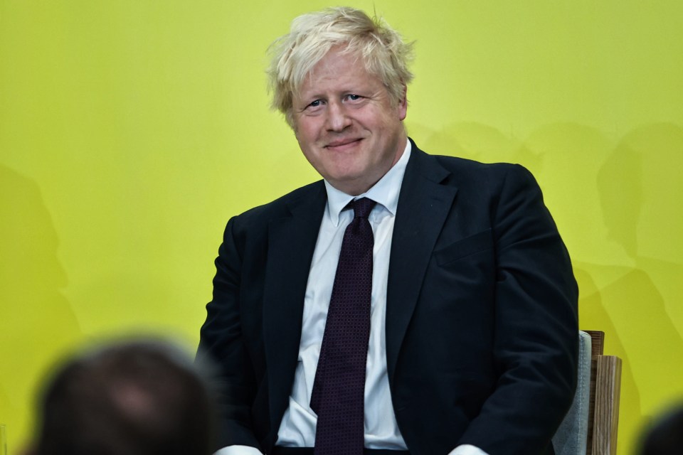 a man in a suit and tie smiles in front of a yellow background