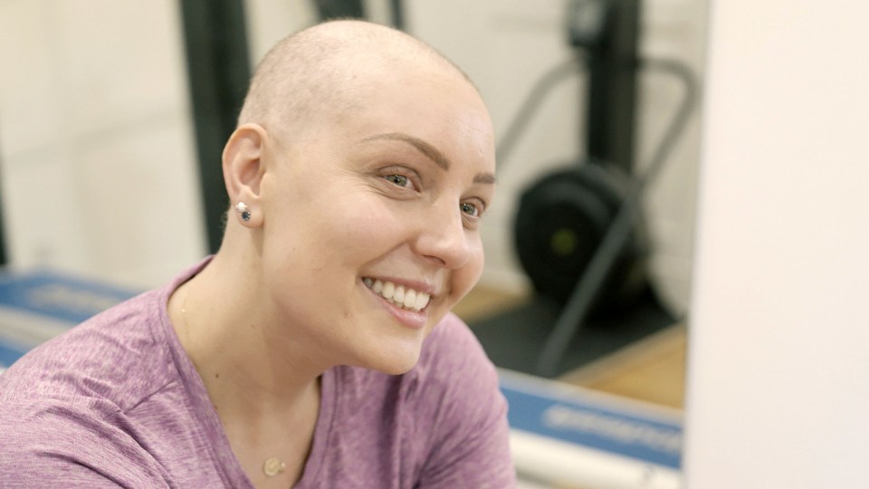 a woman with a shaved head is smiling in front of a treadmill