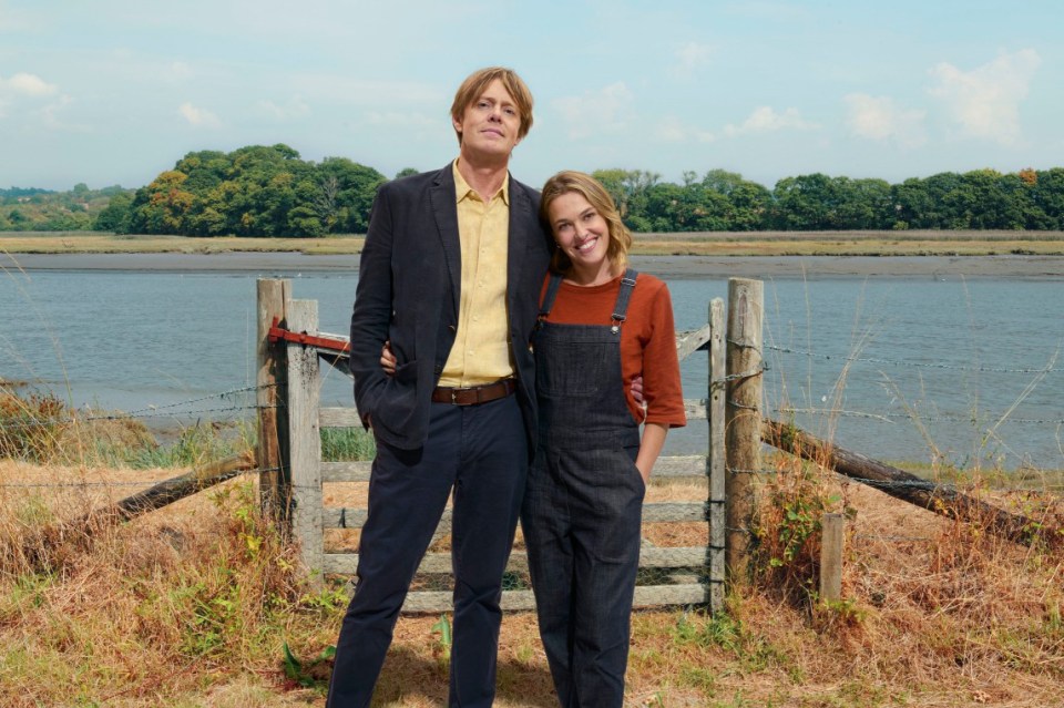 a man in a suit and overalls stands next to a woman in overalls