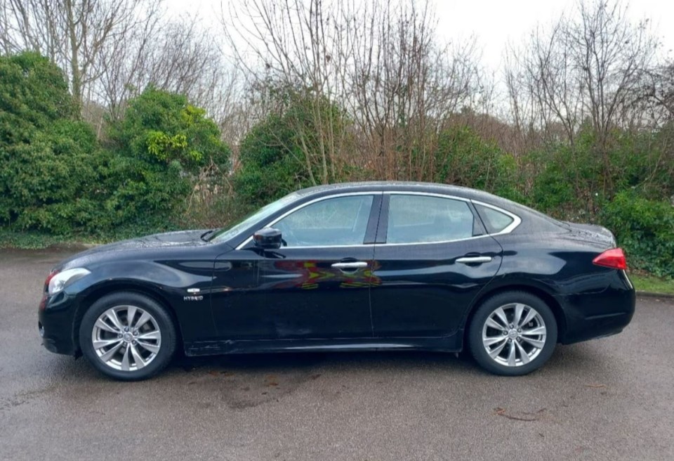 a black car is parked in a parking lot with trees in the background
