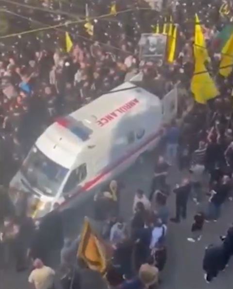 an ambulance is driving through a crowd of people on a street .