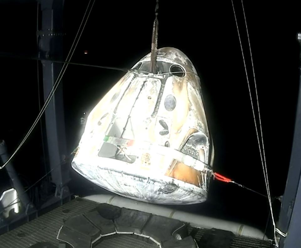 a space capsule is being lifted by a crane at night