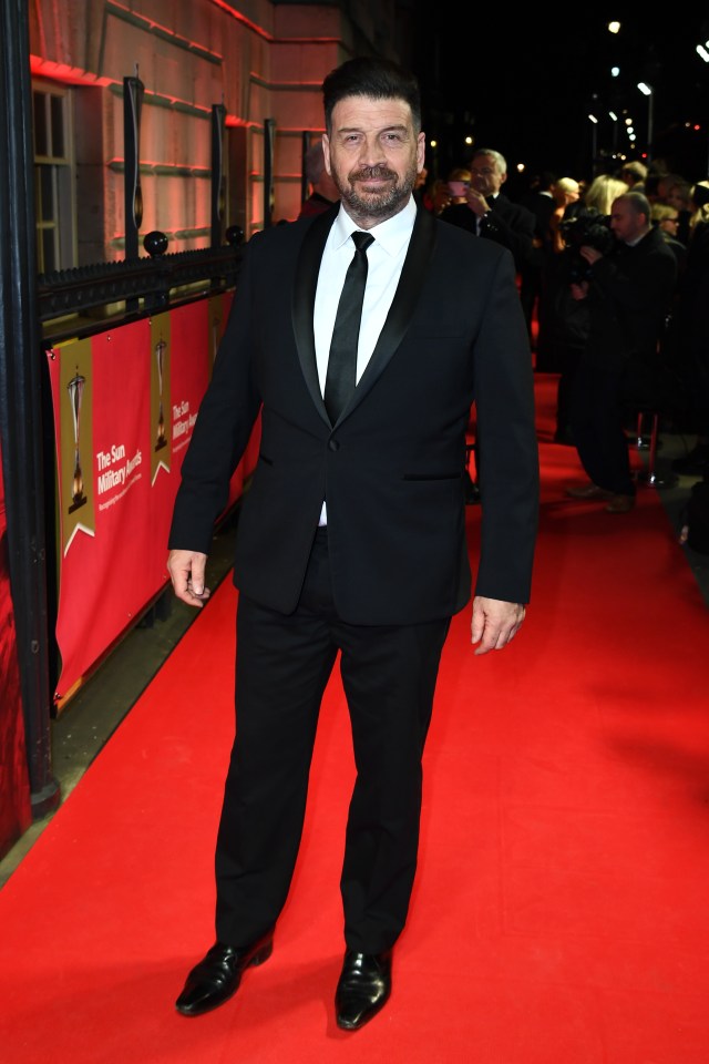 a man in a tuxedo stands on a red carpet in front of a banner that says the sun military awards