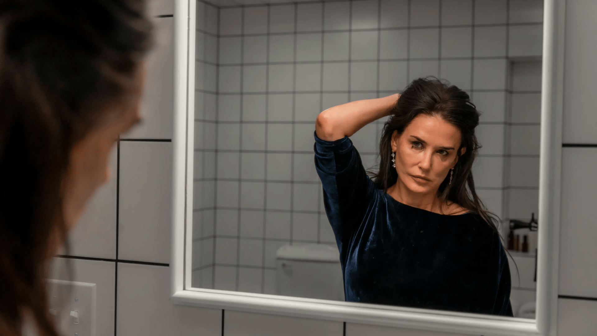 a woman looks at her reflection in a bathroom mirror