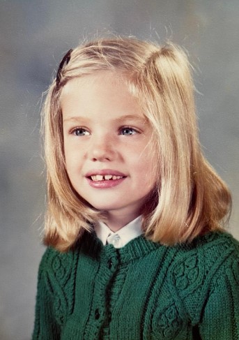 a young girl with blonde hair wearing a green sweater