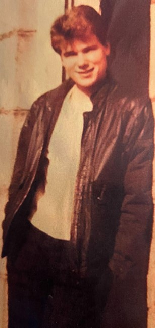 a young man wearing a leather jacket is leaning against a wall