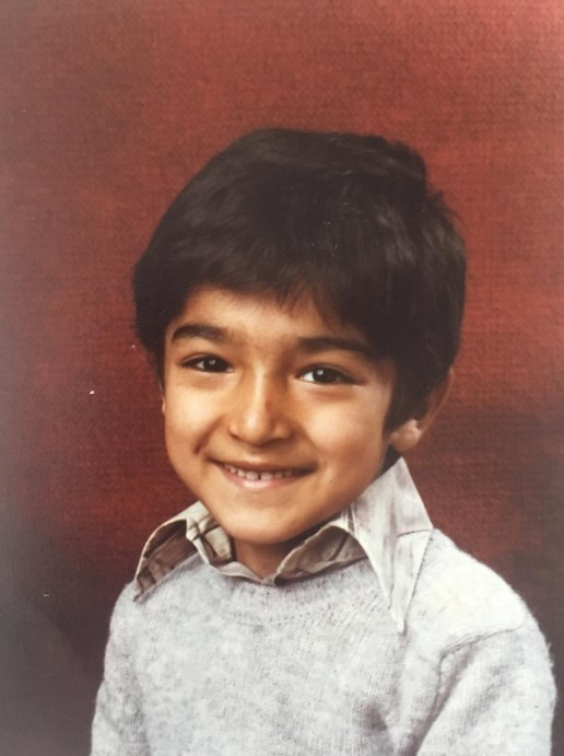 a young boy wearing a grey sweater smiles for the camera