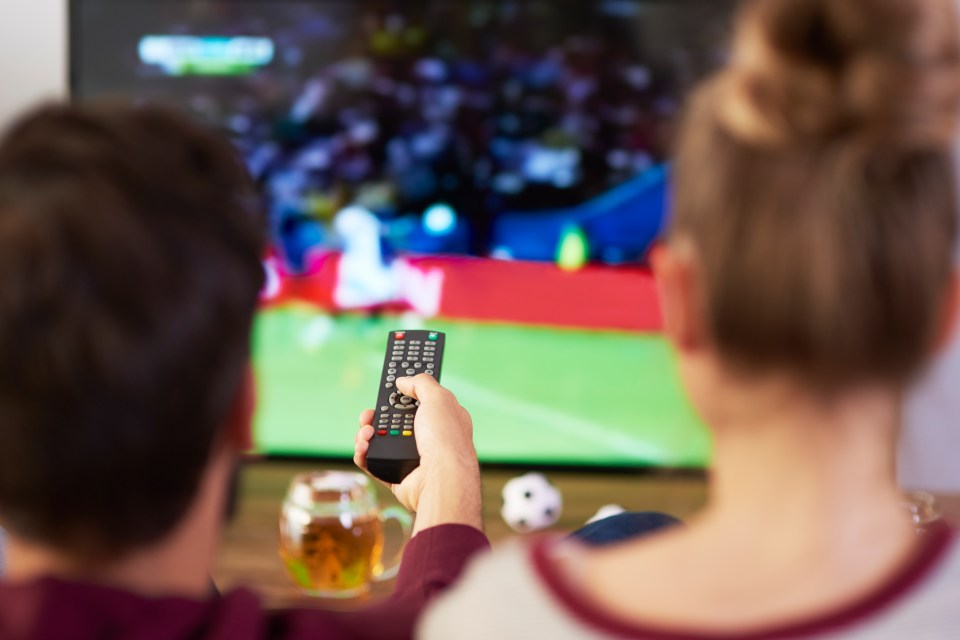 a man is holding a remote control while watching a soccer game