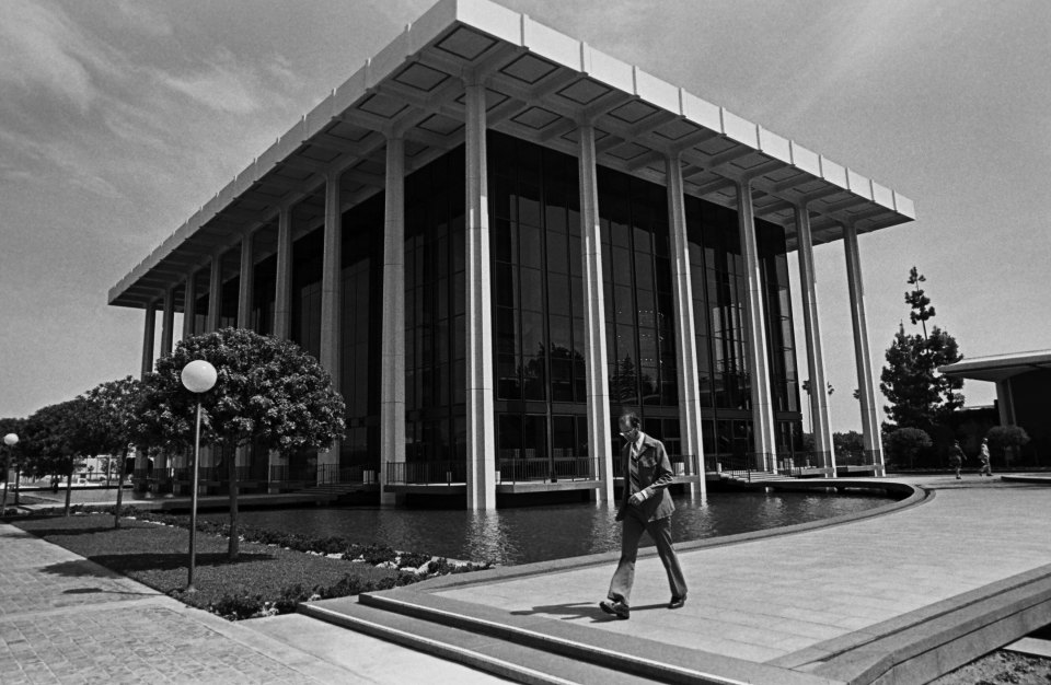 a black and white photo of a man walking in front of a large building