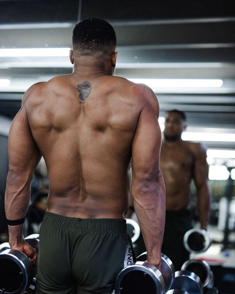 a man with a tattoo on his back holds dumbbells in front of a mirror
