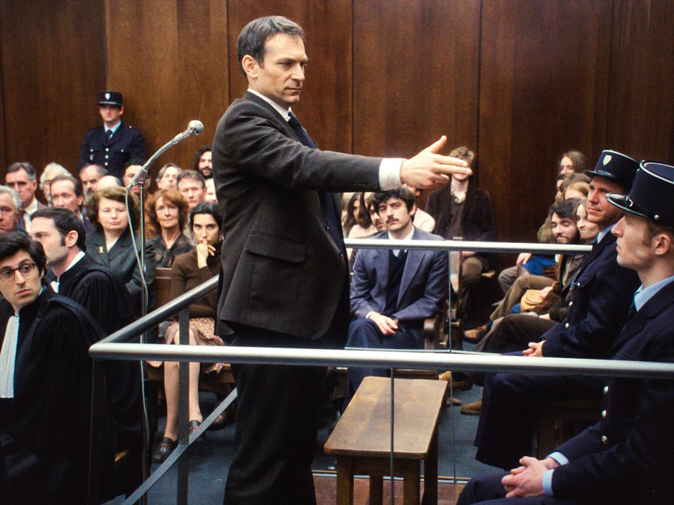 a man in a suit stands in front of a microphone in a courtroom