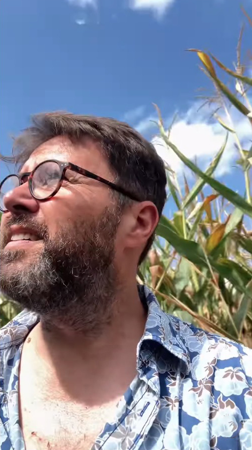 a man with glasses and a beard is standing in a field
