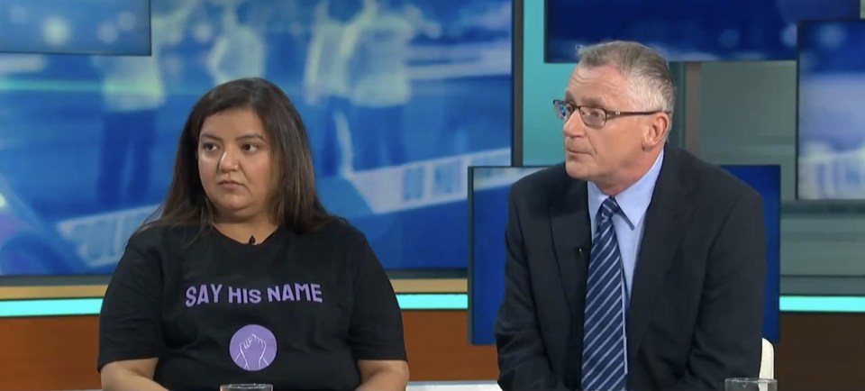 a woman wearing a shirt that says say his name sits next to a man in a suit