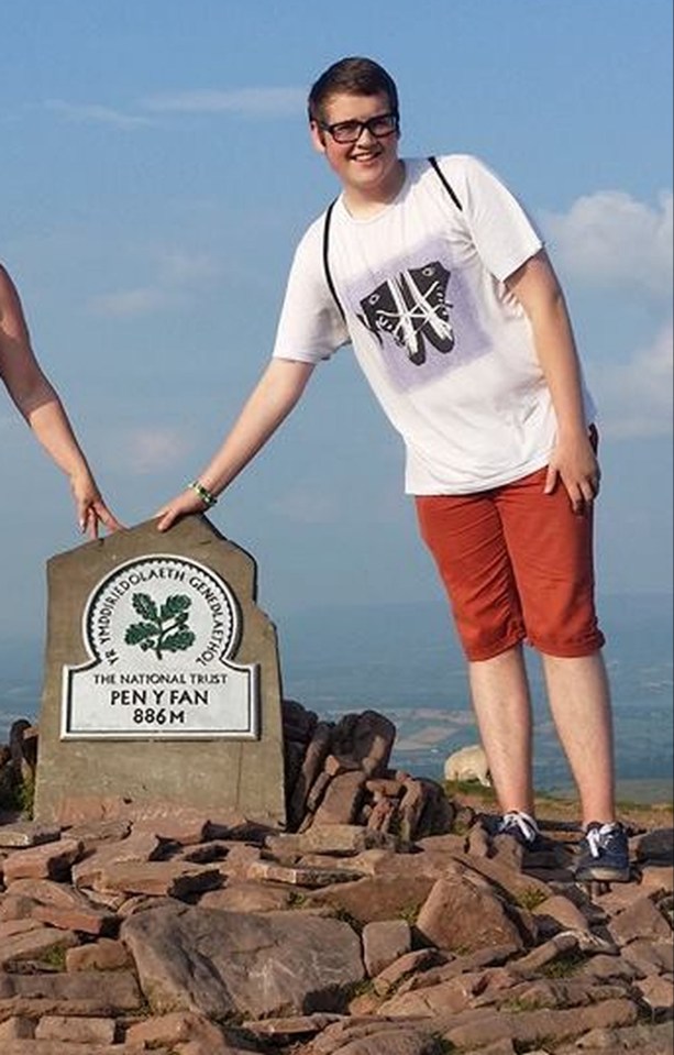 a young man stands on top of a rocky hill next to a sign that says pen y fan
