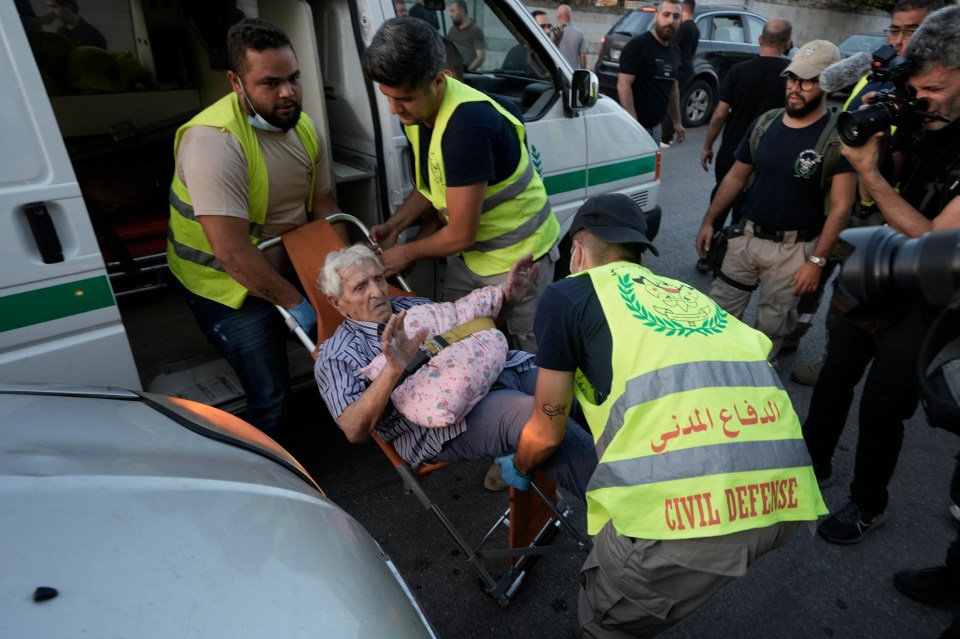 Civil defense workers carry an elderly citizen who fled from the south as he arrives at a school turned into a shelter in Beirut