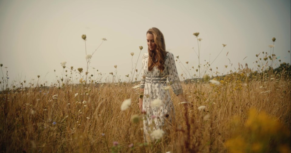 a woman in a white dress stands in a field of tall grass