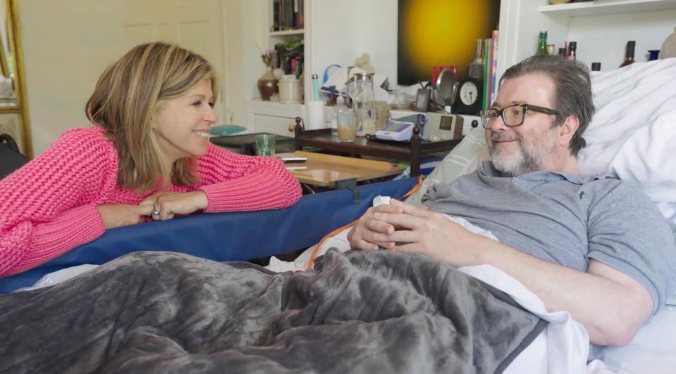 a woman in a pink sweater talks to a man in a hospital bed